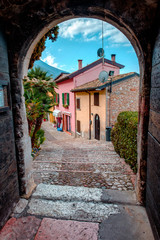 Naklejka premium View of the street with colored houses from a dark arch. The city of Malcesine. Italy.