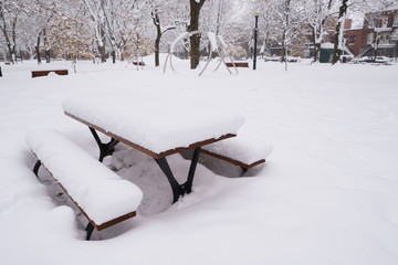 First snow has fallen on everything during the night.  A picnic table is covered of snow in a public park.