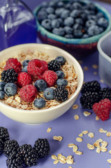 Healthy breakfast. White plate with oatmeal strewn and different berries on a blue background.