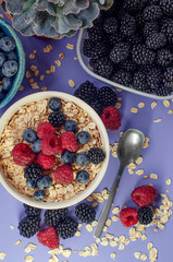 Healthy breakfast. White plate with oatmeal strewn and different berries on a blue background.