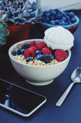 Healthy breakfast. White plate with oatmeal strewn and different berries on a blue background. Summer harvest.