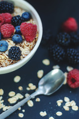 Healthy breakfast. White plate with oatmeal strewn and different berries on a blue background.