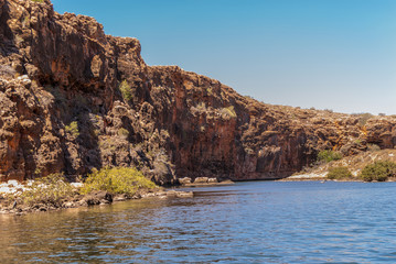 Exmouth, Western Australia - November 27, 2009: Yardie Creek Gorge in Cape Range National Park on North West Cape. Wide shot of Red rock cliffs between blue water and sky. Some green vegetation.