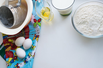 ingredients for pancakes are laid out on a multi-colored tablecloth, raw ingredients: eggs, milk, oil, flour, copy space