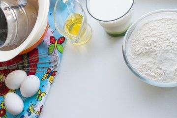 ingredients for pancakes are laid out on a multi-colored tablecloth, raw ingredients: eggs, milk, oil, flour, copy space