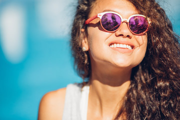 Positive summertime portrait of stylish girl having fun near pool, trendy outfit and sunglasses, traveling vibes, amazing view on luxury pool.Sexy perfect fit body woman. Copy, empty space for text