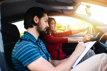 Driving school or test. Beautiful young woman learning how to drive car together with her instructor