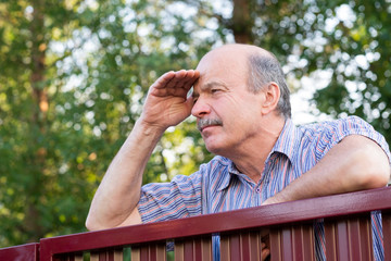 Mature caucasian man carefully watching over the fence.