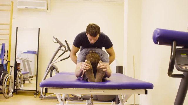 Doctor physiotherapist doing recovery exercises for young disable man at the rehabilitation clinic