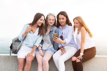 A group of students in the Park. A beautiful brunette woman shows something to her friends on her smartphone