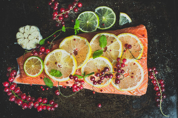 Uncooked salmon fillet with sliced lemon and red currants on top. Flat lay