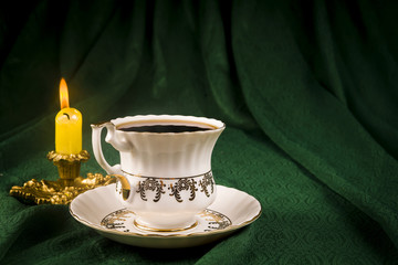 A lit candle with a retro cup, against a green cloth