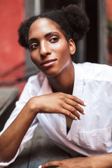 Portrait of beautiful african lady with dark curly hair in white shirt dreamily looking aside