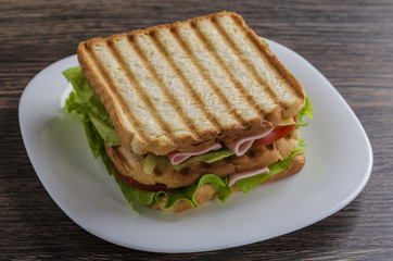 Close up of fresh sandwich with ham, bacon,tomatoes on white plate