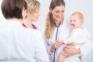 Dedicated female physician holding a cute baby girl in her arms during routine visit in a modern pediatric center with friendly and experienced specialists