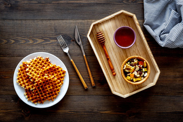 Round belgian waffles for breakfast. Breakfast in bed. Waffles on plate. Honey and dried fruits in tray, knife and fork, tablecloth on dark wooden background top view copy space