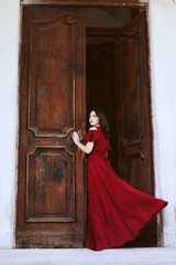 Beautiful woman in a red dress standing near a big wooden door.