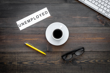 Unempoyed sign on office desk with computer keyboard on dark wooden background top view. Unemployment concept
