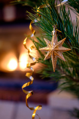 A large goden star toy. Christmas toys on the Christmas tree near the burning fireplace. Christmas toys in the form of golden shiny star.