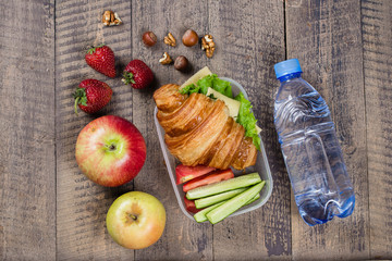 Back to school concept. Lunch box with croissant, fruits and vegetables on wooden background. Copy space, top view