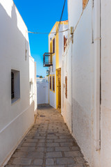 Fototapeta na wymiar Typical Greek narrow street with white houses on Rhodes island. Lindos village, Dodecanese, Greece.