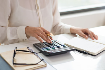 Closeup of woman calculating expenses. Notebooks, glasses and calculator lying on desk. Finance...
