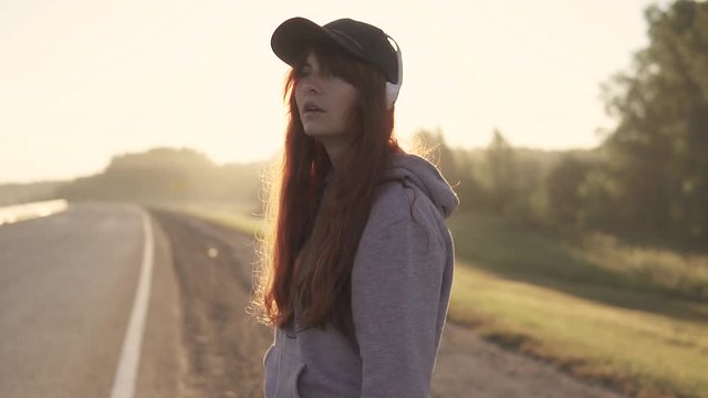 close-up portrait of a red-haired girl with a piercing in her nose and lips and headphones. On the Sunset. slow motion
