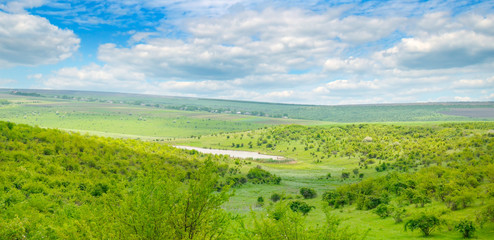 Green field and blue sky. Picturesque hills formed by an old river terrace. Moldova. Agricultural landscape. Wide photo.
