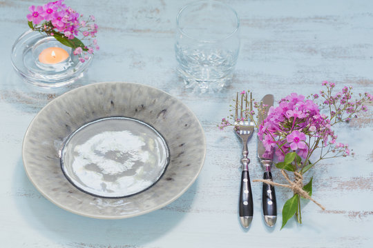 Rustic table setting with pink flowers, empty glass and candle on light wooden table.