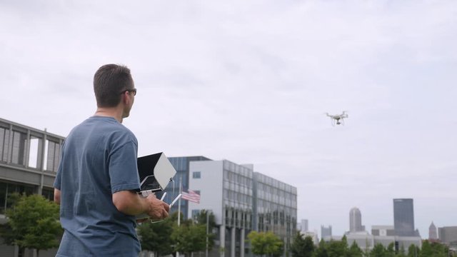 A remote pilot flies an unmanned drone outside near an office park. The Pittsburgh, Pennsylvania skyline is seen in the distance. Shot at 60fps slow motion.  	