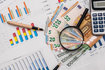 Obraz premium Euro banknotes with magnifier and calculator on business graphs