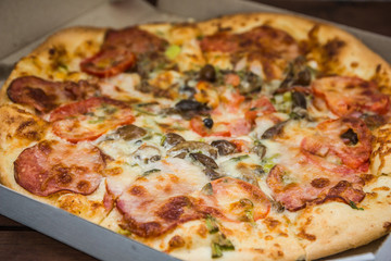 Pizza on wooden boards in rustic style. Italian pizza in a cardboard box. Simple food on a wooden background. Tasty dish for lunch