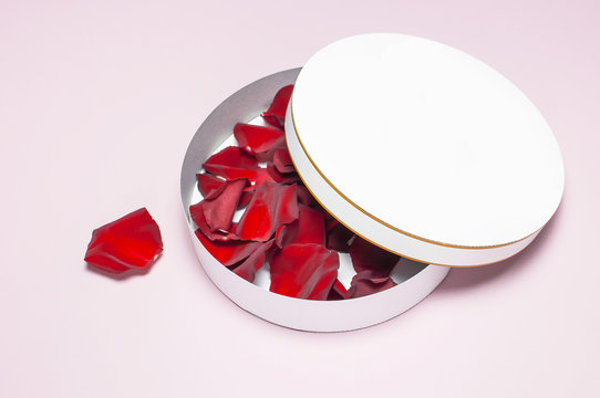 Round white cardboard blank box with red rose petals top view flat lay. Mock up on pink background. Packaging design, an empty box for shopping.