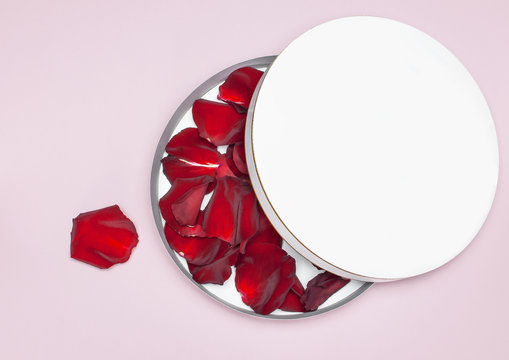 Round white cardboard blank box with red rose petals top view flat lay. Mock up on pink background. Packaging design, an empty box for shopping.