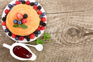 Pancakes stack with different berries on old wooden background with copy space for your text. Top view. Flat lay