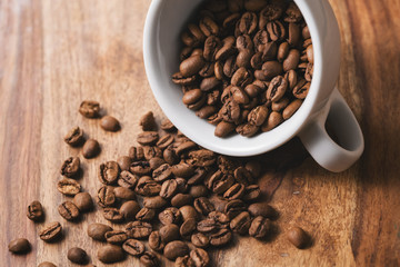 Overturned coffee cup with coffee beans on wood table