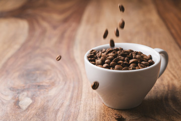 Coffee beans falling into coffee cup on wood table