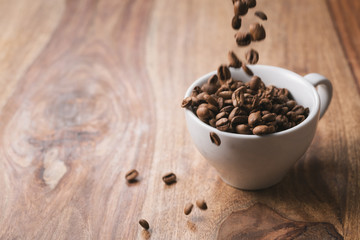 Coffee beans falling into coffee cup on wood table