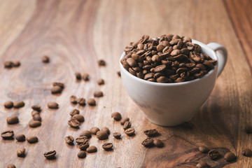 Coffee beans falling into coffee cup on wood table