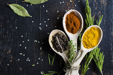 White spoons with spices are on a black wooden table