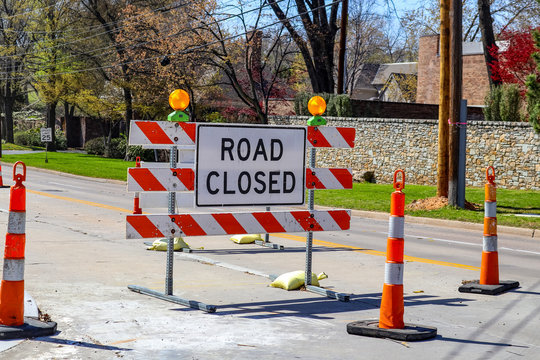 Road closed sign in the middle of four lane highway in residential neighborhood in early spring