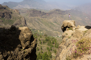 Fearless man jumping high up on rock edge in Roque Nublo natural park, Gran Canaria. Young climber celebrating on mountain peak. Risk, danger, dare,  brave adventurer concepts
