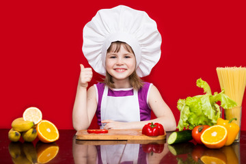 Happy little girl in chef uniform cuts vegetables in kitchen. Kid chef. Vegetarian. Cooking Process Concept