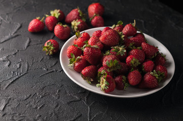 Fresh strawberries in a plate on a black background.