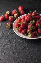 Fresh strawberries in a plate on a black background.