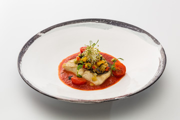 piece of fish with stewed vegetables in a plate isolated on white background