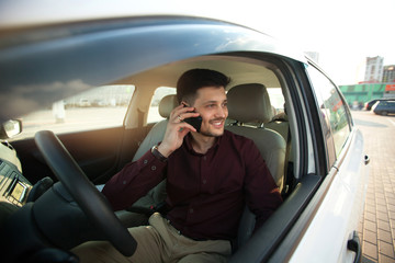 beautiful young guy in a shirt sitting in the car and talking on the phone