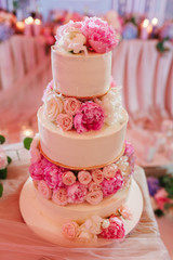 Obraz na płótnie Canvas White wedding cake decorated with peony roses on pink restaurant background