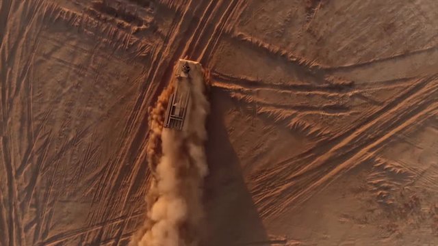 View from above of a military vehicle driving through the desert at sunset