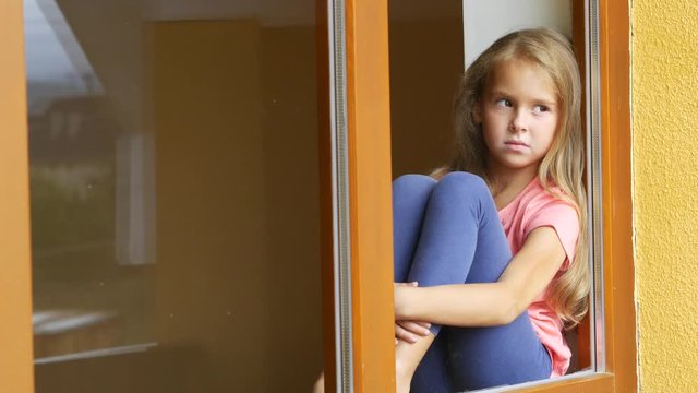 A shy girl sitting by the window, looking at the street and waving greetings to someone.